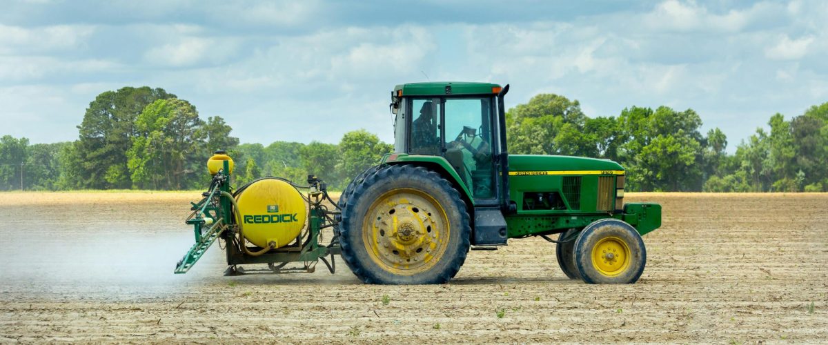 Green tractor with sprayer working in an open farm field under a cloudy sky.